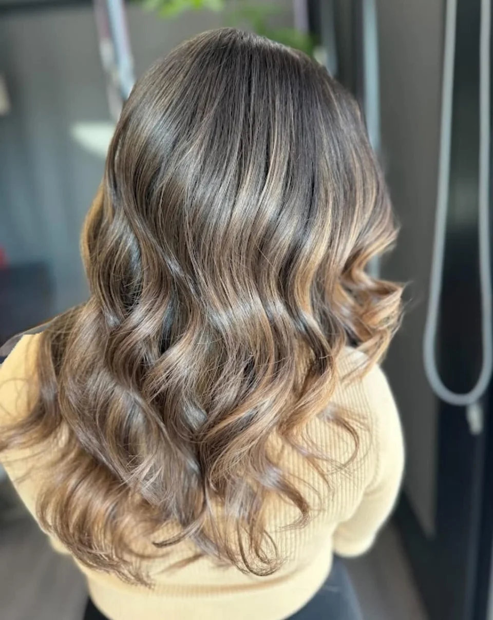 Dimensional brunette hair with caramel highlights styled in soft waves