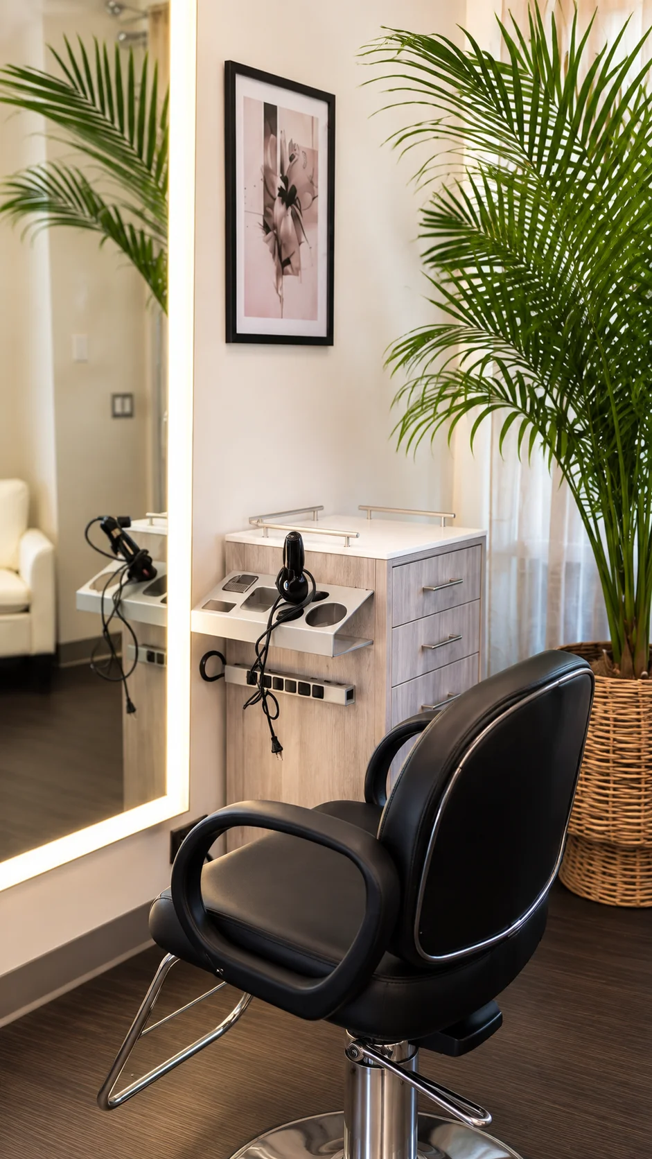 Black styling chair beside a lit mirror and palm